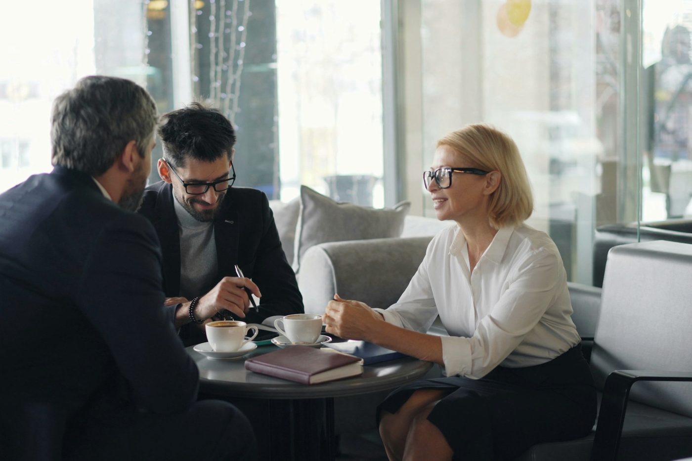 Three people in a meeting over coffee, one taking notes.