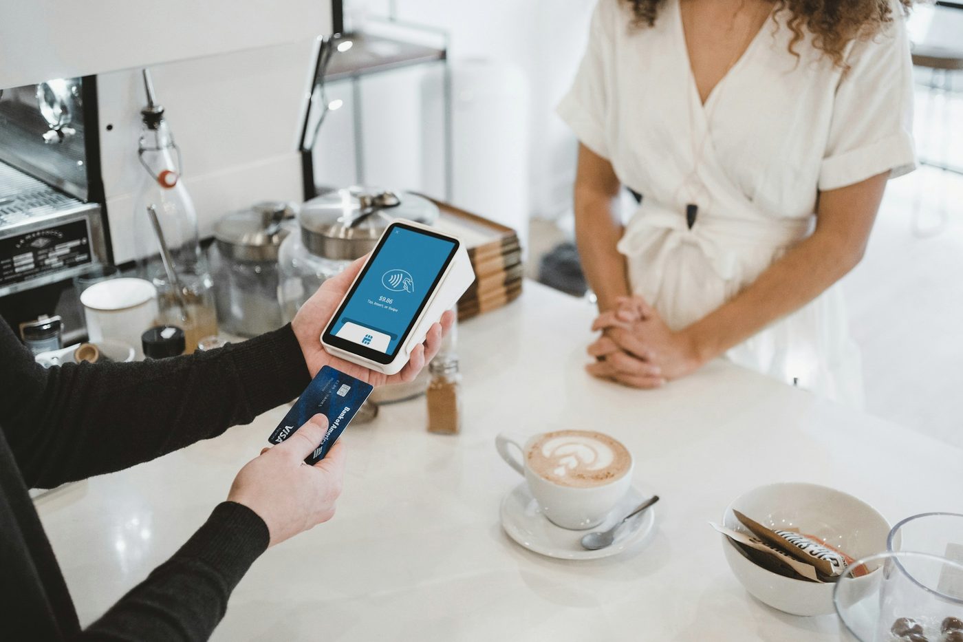 A customer paying by card on a handheld reader at a café counter.
