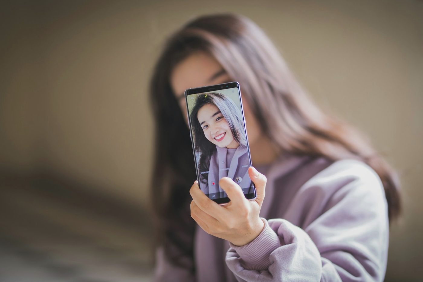 A person holding up a phone that shows their own face, as in a selfie check.